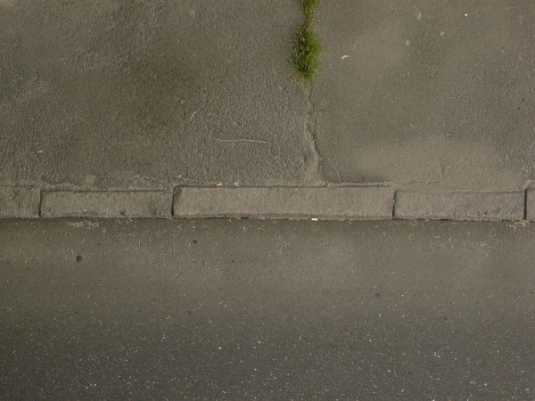 Road edge texture, dark grey in color and of varying degrees of roughness, separated in the center by a stone divider. Small amounts of grass and debris are present.